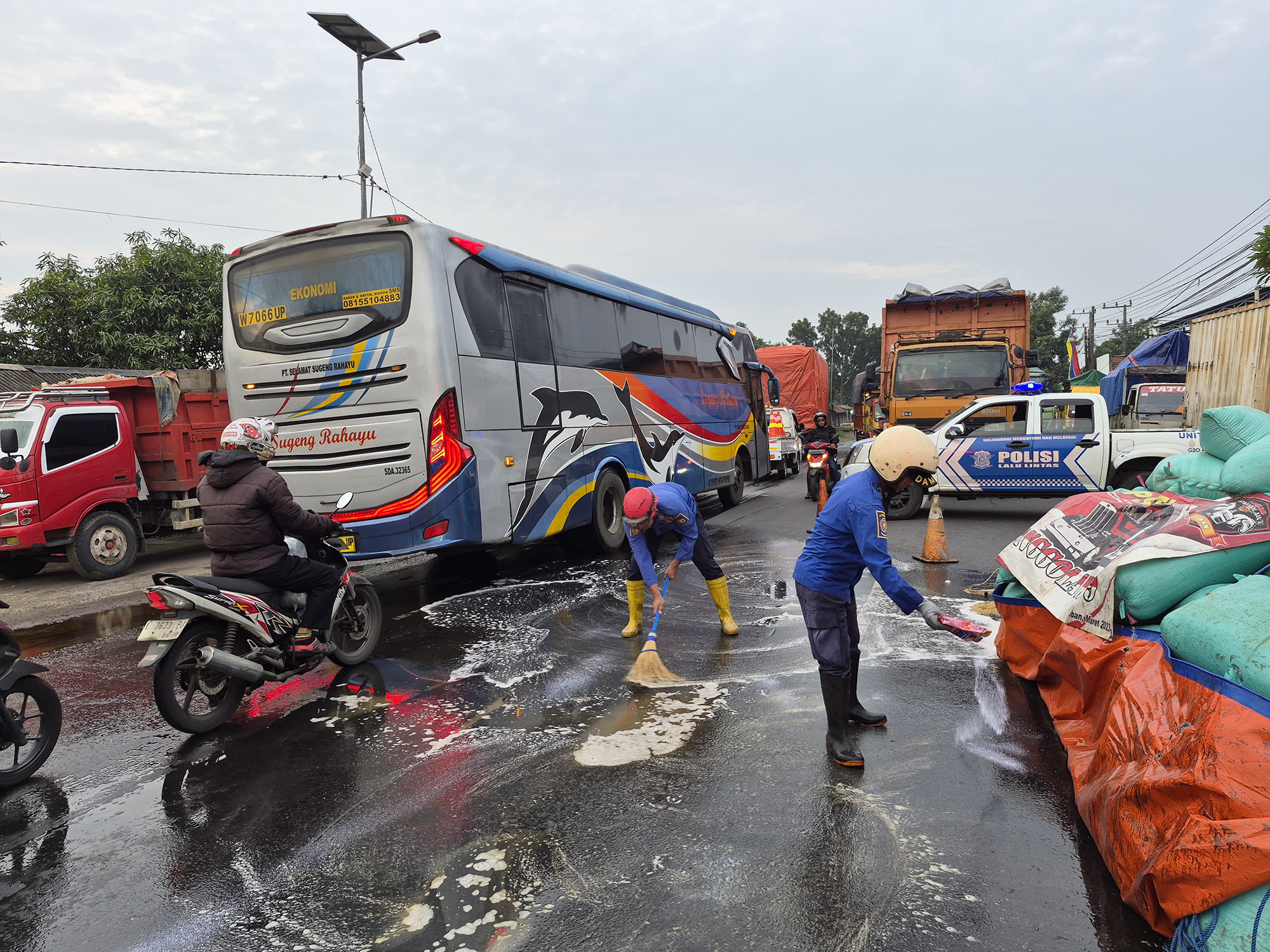Petugas Pemadam Kebakaran membersihkan tumpahan solar di Jalan Panglima Sudirman Perak Jombang yang sebabkan truck tergelincir. (Foto : ist)